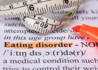 Close-up of a book page with a pink highlighted text 'Eating disorder' and a measuring tape wrapped around an orange marker.