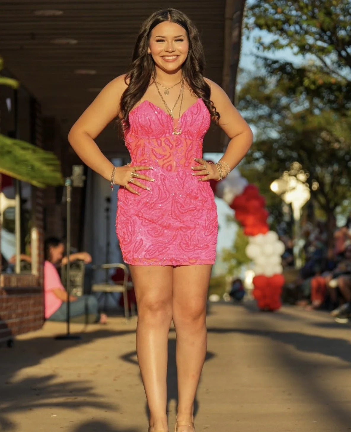 Woman smiling in a pink dress walking outdoors at an event.