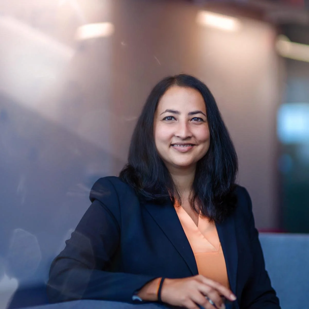 A woman with shoulder-length black hair smiling in a professional setting, wearing a dark blazer and peach-colored blouse.