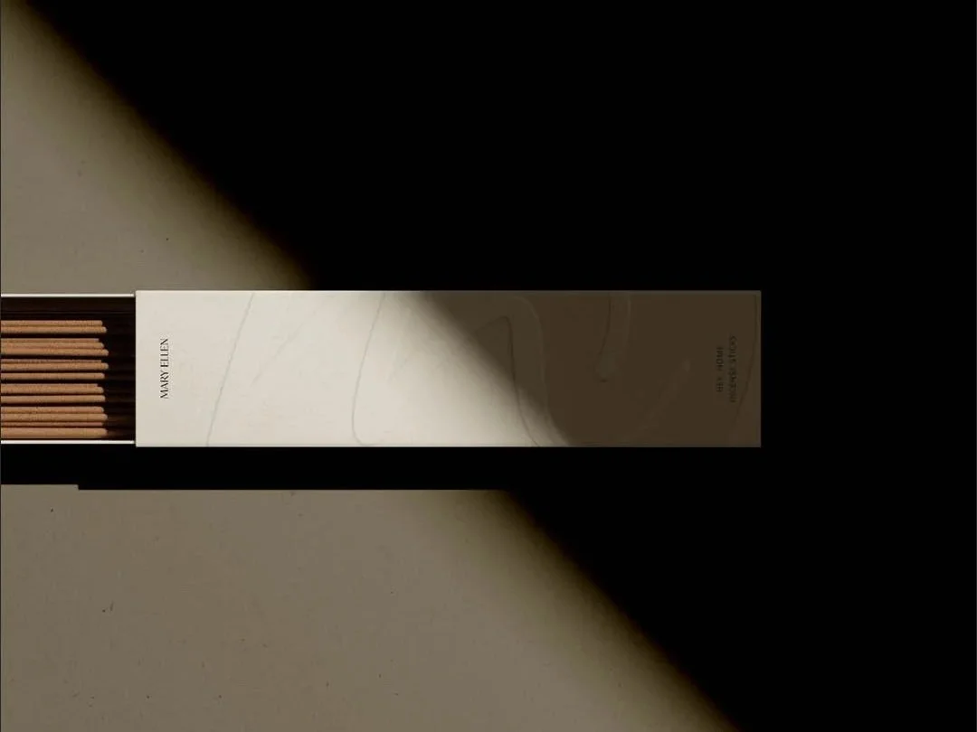 A box of matches labeled 'Mary Ellen' lying on a beige surface, with shadows cast across the scene.