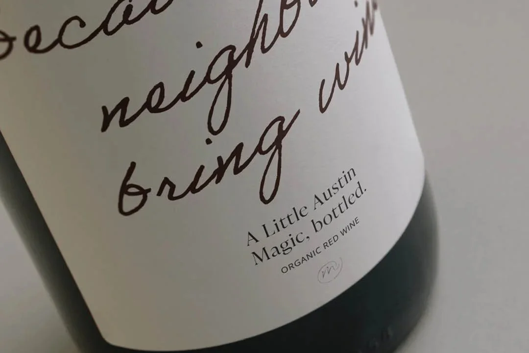 Close-up of a wine bottle with a white label featuring handwritten-style text and printed text indicating it is an organic red wine from Austin, Texas.
