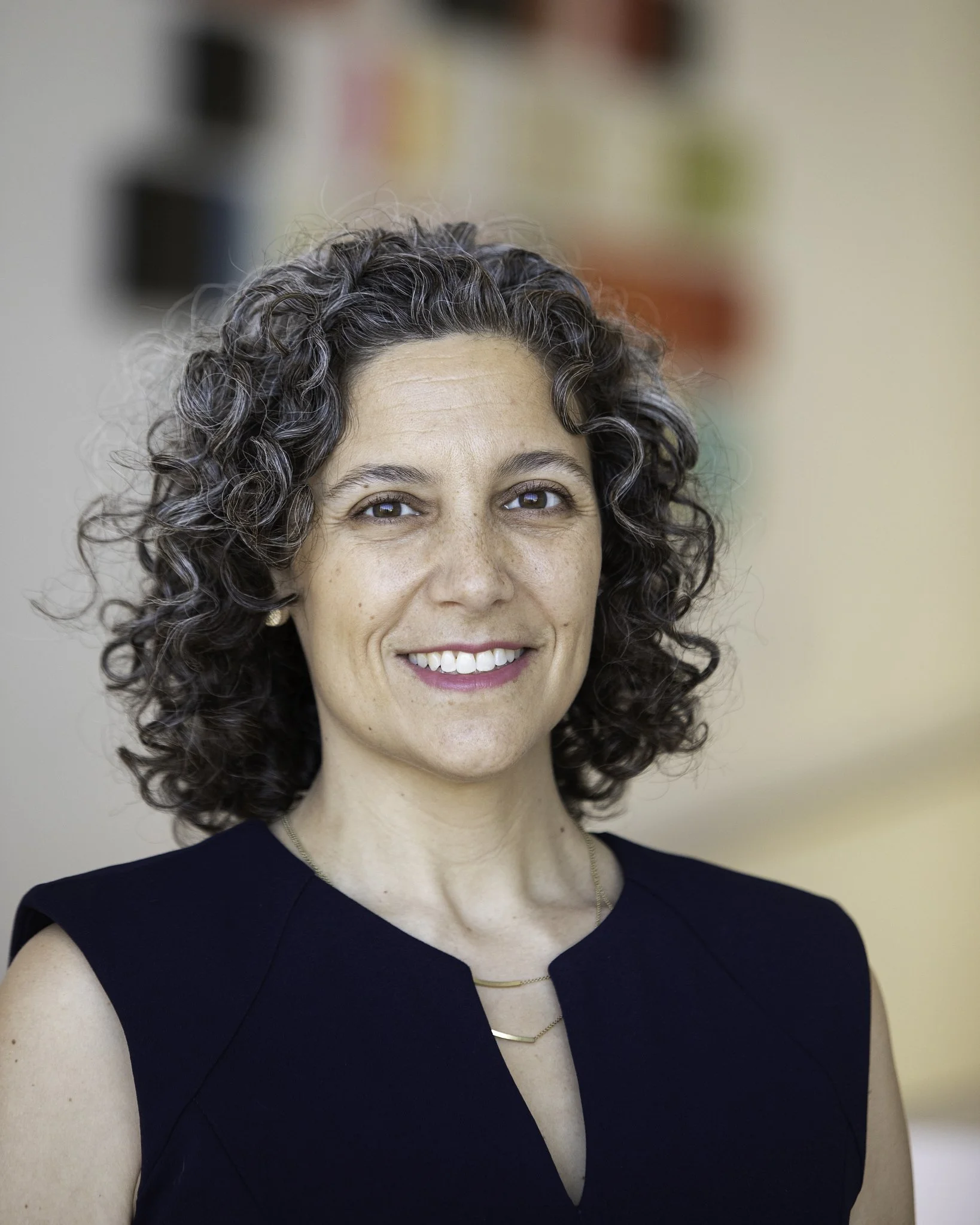 Headshot of a woman with curly hair smiling against a gray background.