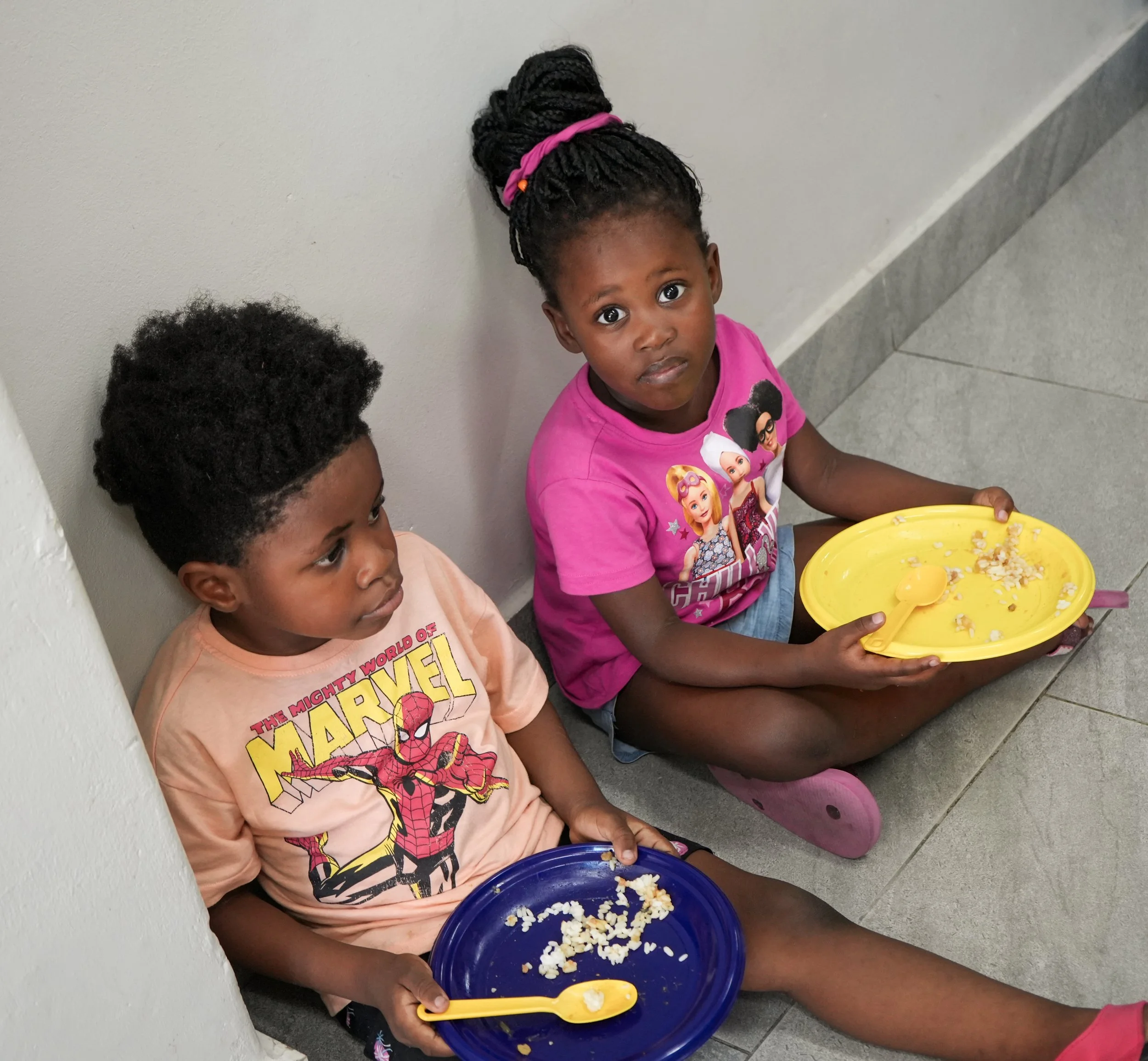 Ein Mädchen und ein Junge sitzen auf dem Boden und haben ihr Mittagessen ausgegessen..