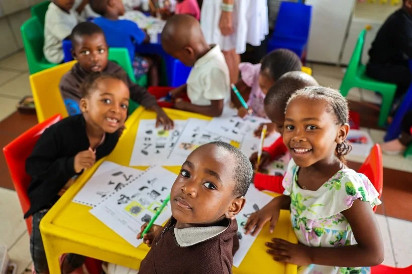 Kinder im Little Lambs Kindergarten in Kapstadt lernen und malen gemeinsam an einem Tisch.