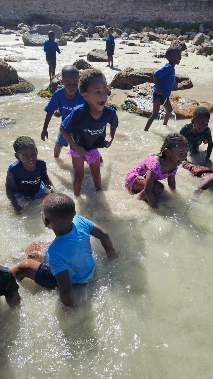 Kinder vom Kindergarten Little Lambs in Kapstadt spielen gemeinsam im Meer.