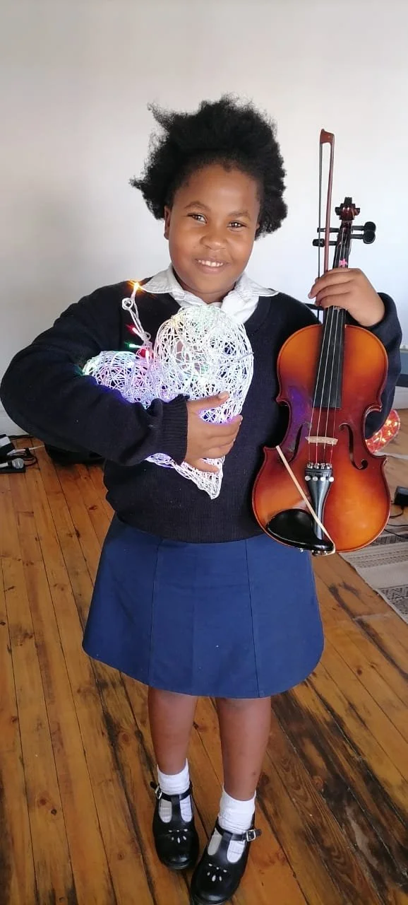 Ein Mädchen lacht mit ihrer Geige und einem grossen Herz in der Hand.