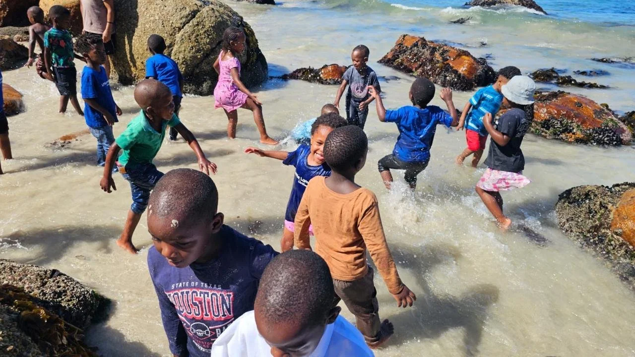 Kinder vom Kindergarten Little Lambs in Kapstadt spielen gemeinsam im Meer.