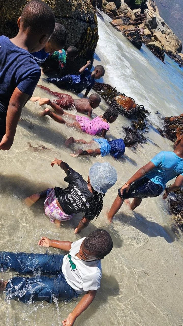 Kinder vom Kindergarten Little Lambs in Kapstadt spielen gemeinsam im Meer.