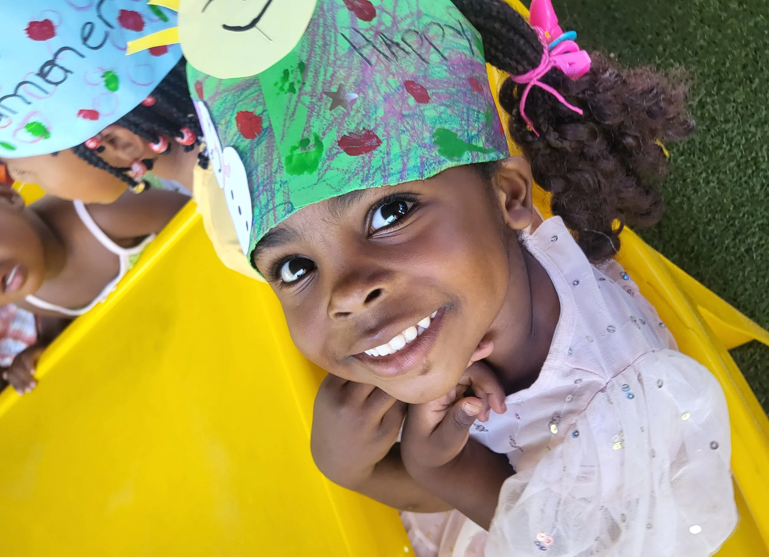 Mädchen lacht mit ihrem selbstgebastelten Hut in die Kamera.