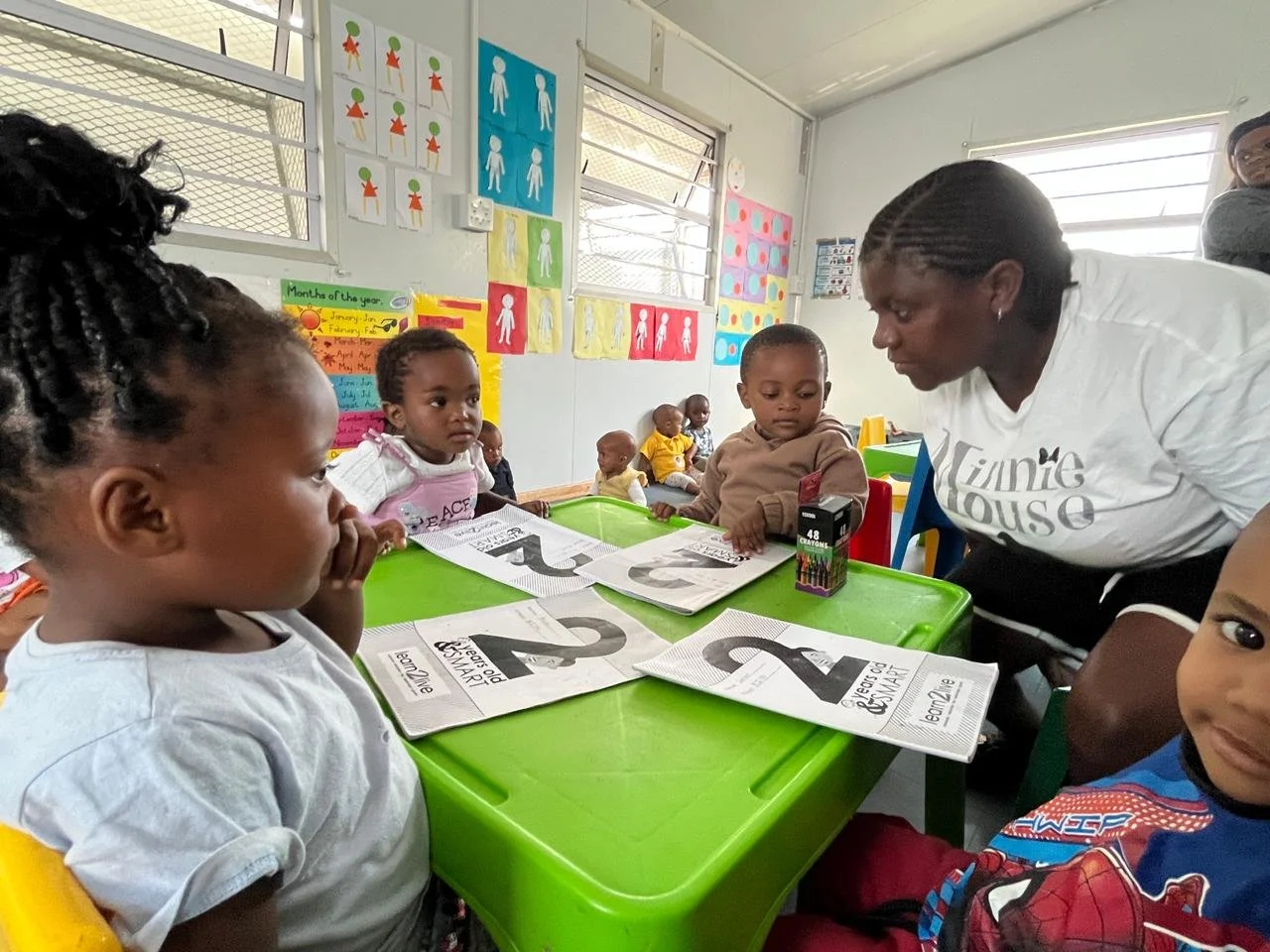 Die Kinder und Lehrerin von True North sitzen an einem Tisch und lernen Zahlen.