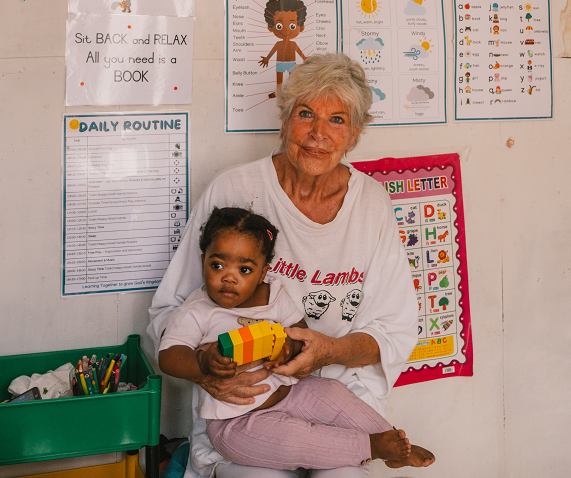 Marlis Schaper, Gründerin und Herz der Kinderhilfe-Kapstadt. hält ein Kleinkind ihn der Hand.