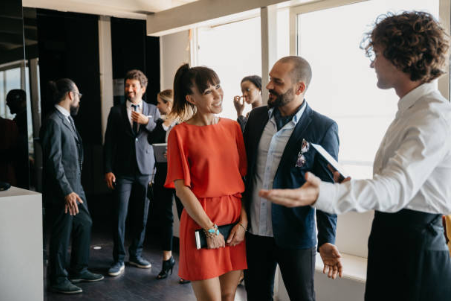 A group of professionally dressed people engaged in conversation at a business or networking event in a modern office space.