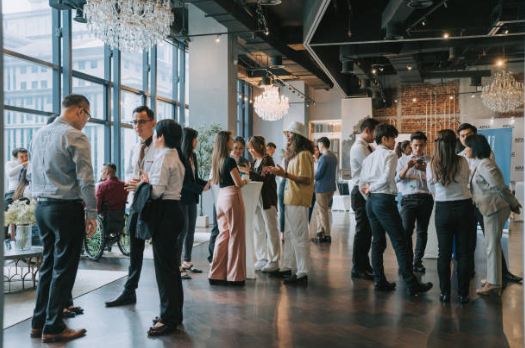 People gathered and networking at a professional event or conference in a modern venue with large windows and chandeliers.