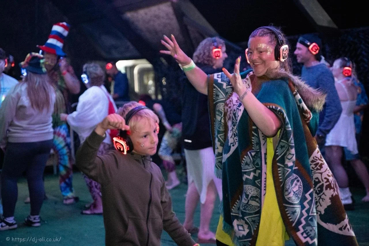 People wearing headphones dancing at a music event, including a woman smiling and dancing with children.