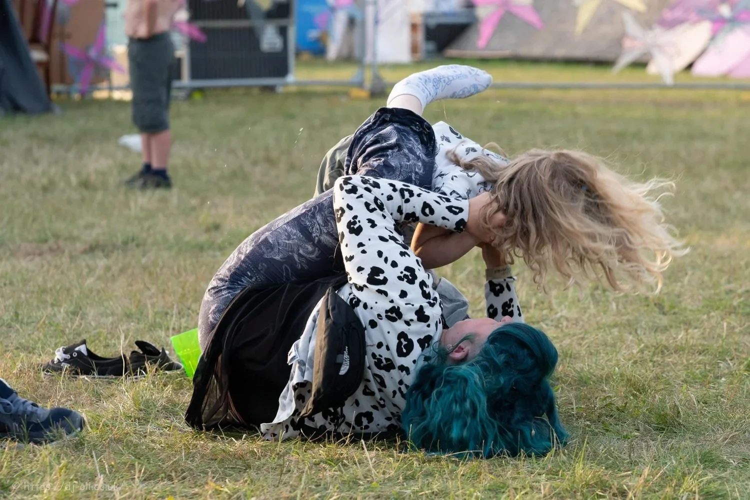 A young women and her young nephew engaging in a playful wrestling match on grass at an outdoor event.