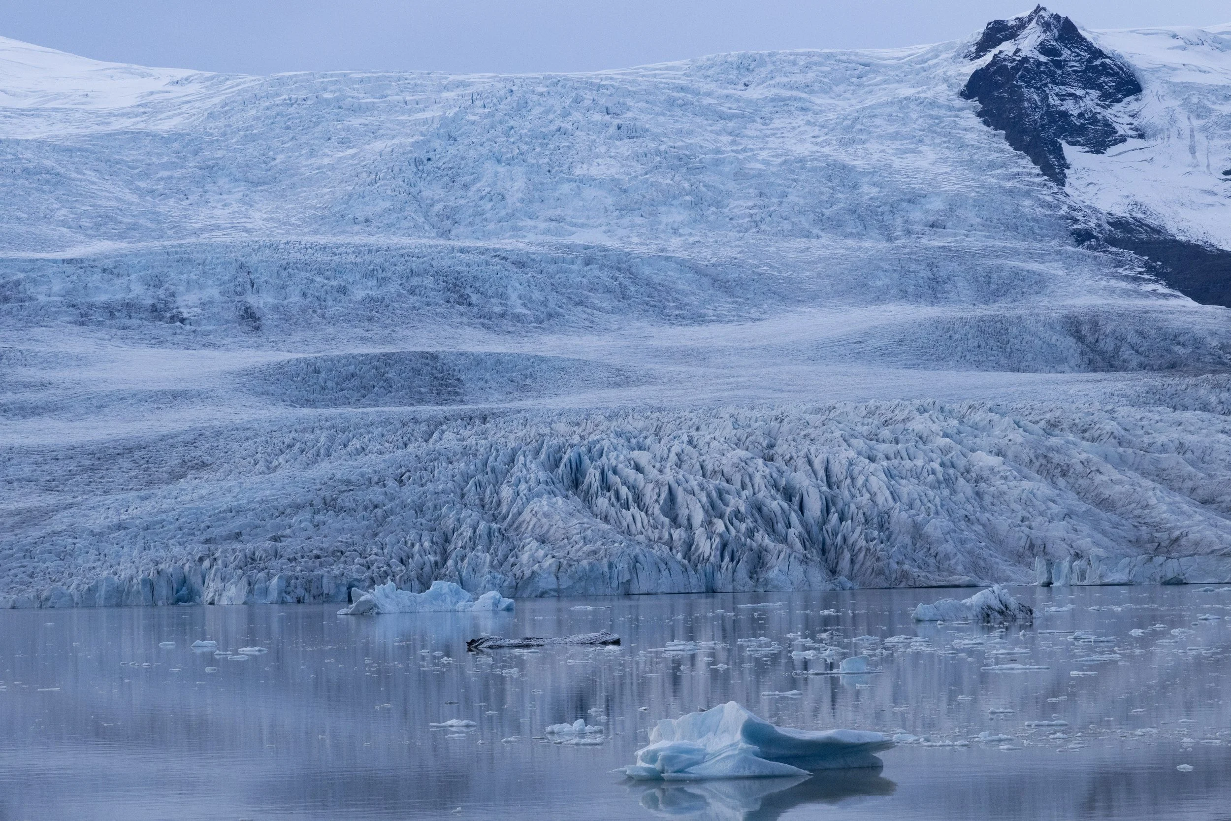 A glacier with ice-covered slopes and floating icebergs in a cold, icy landscape.