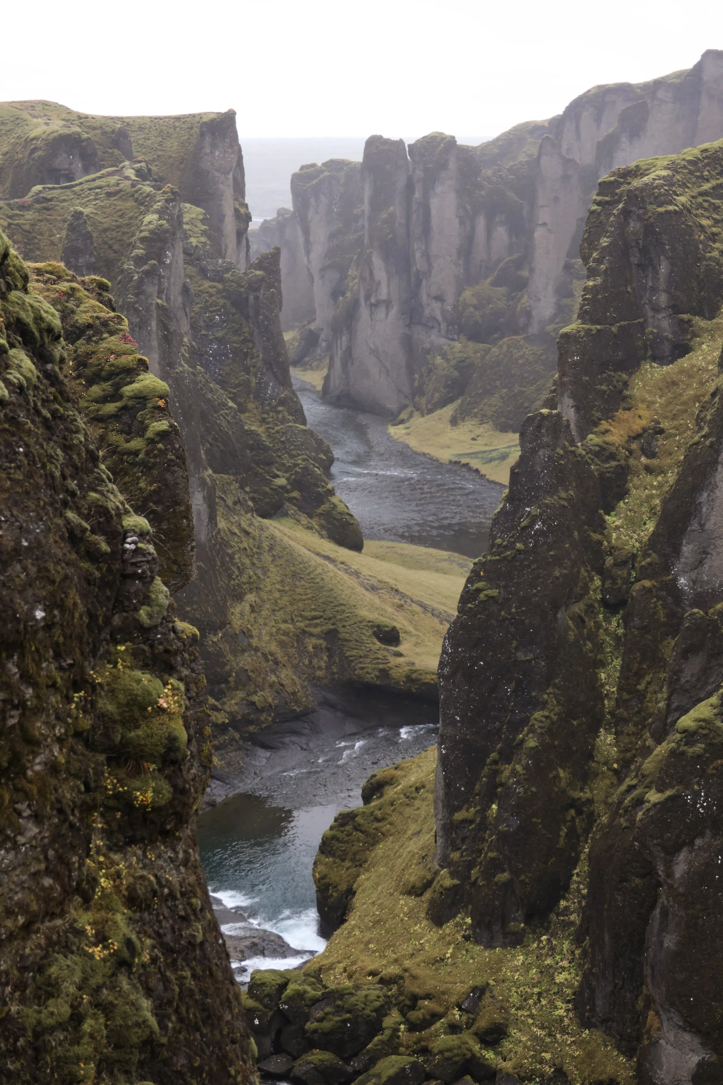 A deep canyon with steep, moss-covered cliffs and a river flowing through the bottom.