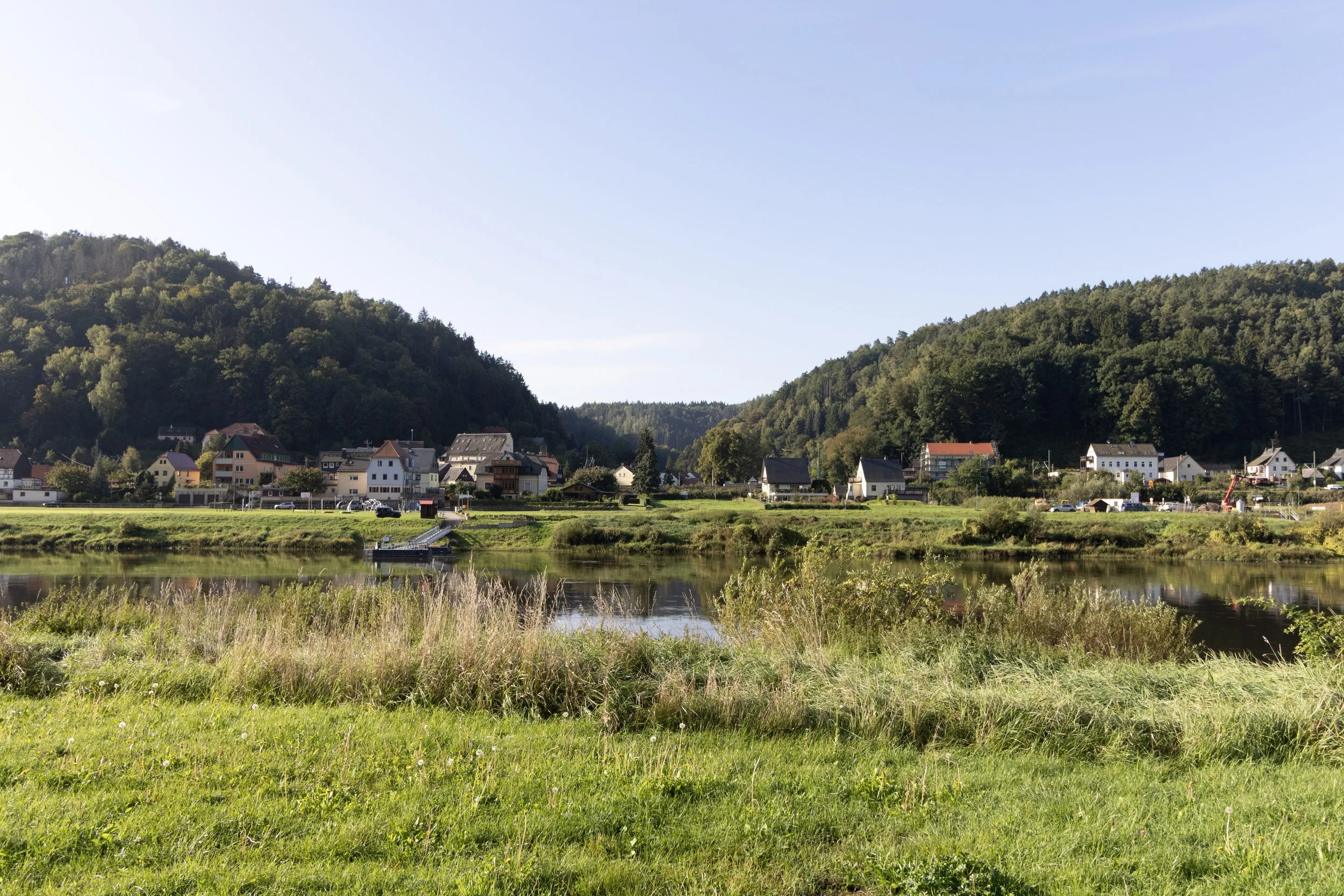 Scenic view of a small town by a river with green hills in the background on a clear day.