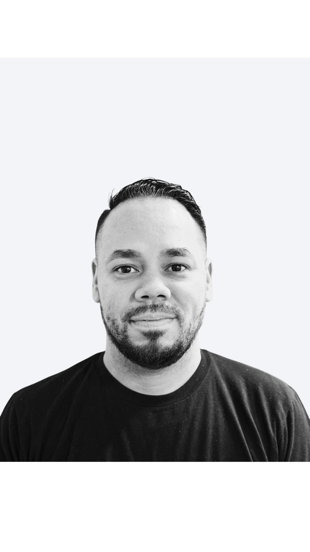 Black and white portrait photo of a man with short dark hair, a beard, and wearing a black t-shirt, smiling slightly.