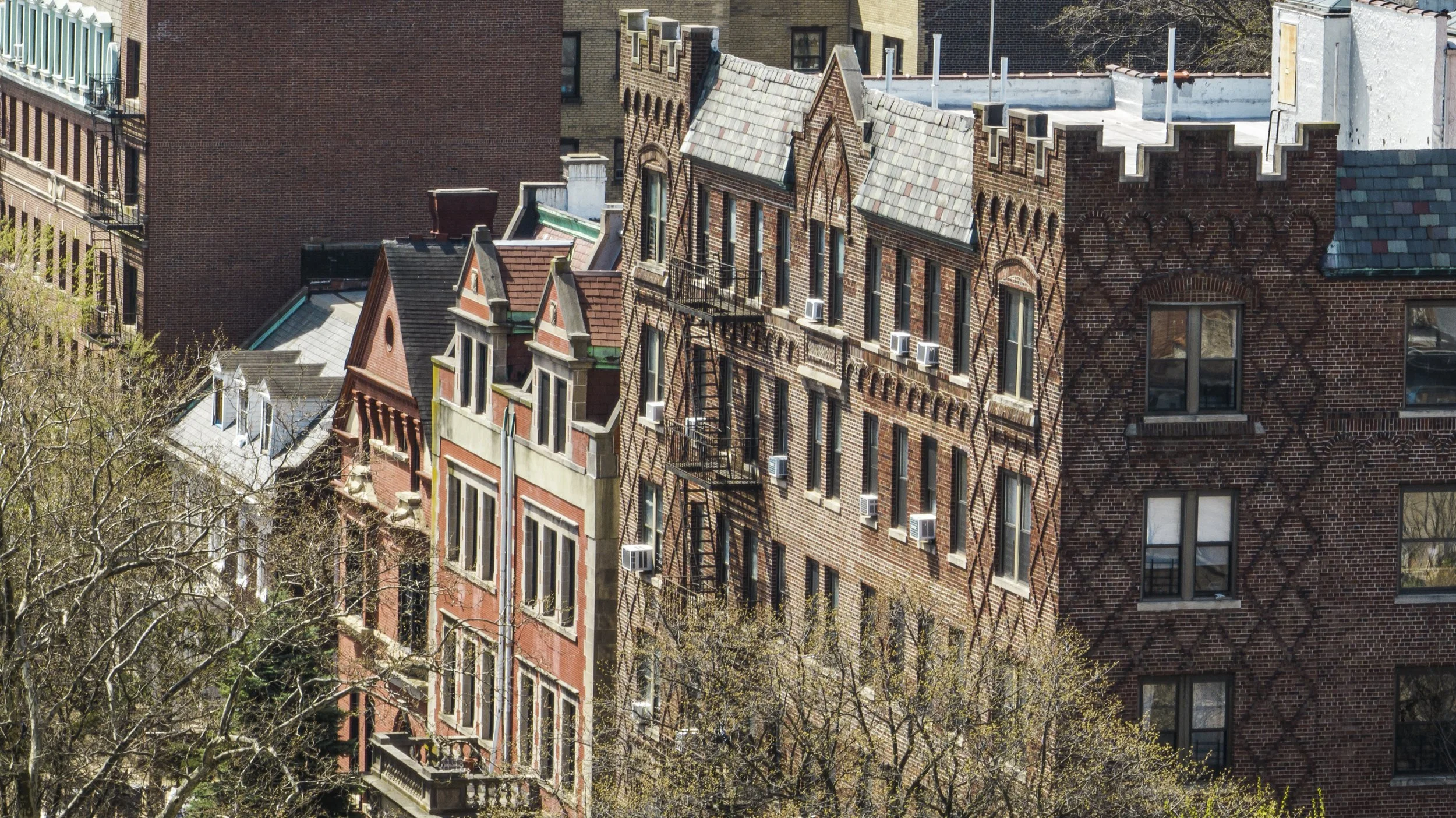 Aerial view of brick residential buildings with fire escapes, surrounded by trees.