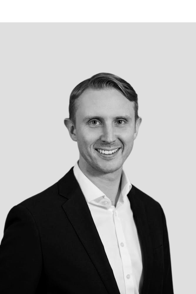 Black and white portrait of a young man in a suit, smiling, against a plain light background.