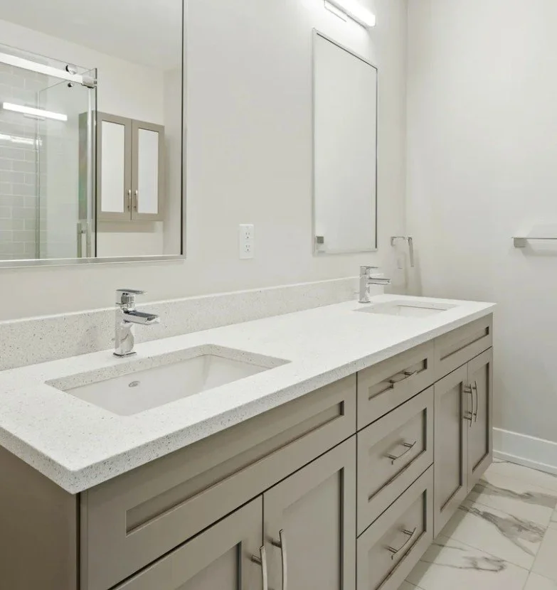 Modern bathroom vanity with dual sinks, light gray cabinet, white countertop, large mirror, wall-mounted cabinet, and towel rack.