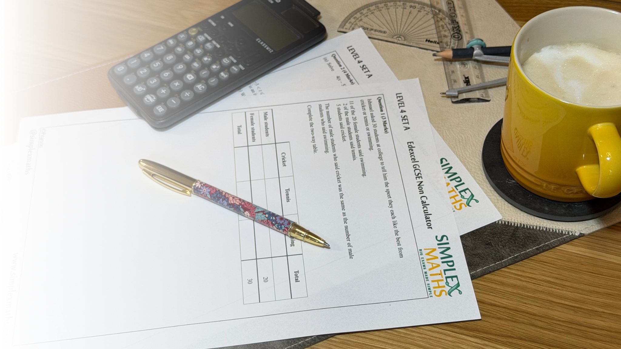 GCSE maths worksheets, calculator, geometry tools and a yellow mug on a desk