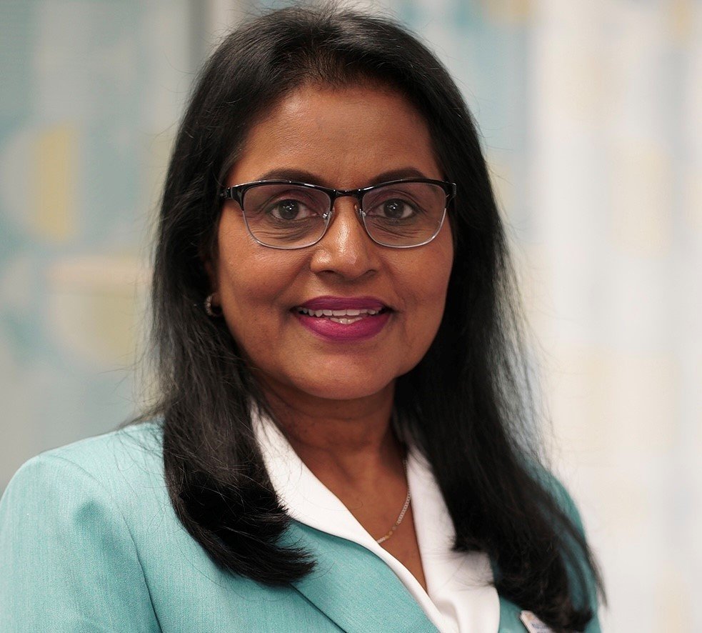 A woman with black hair, glasses, and a turquoise blazer smiling at the camera.