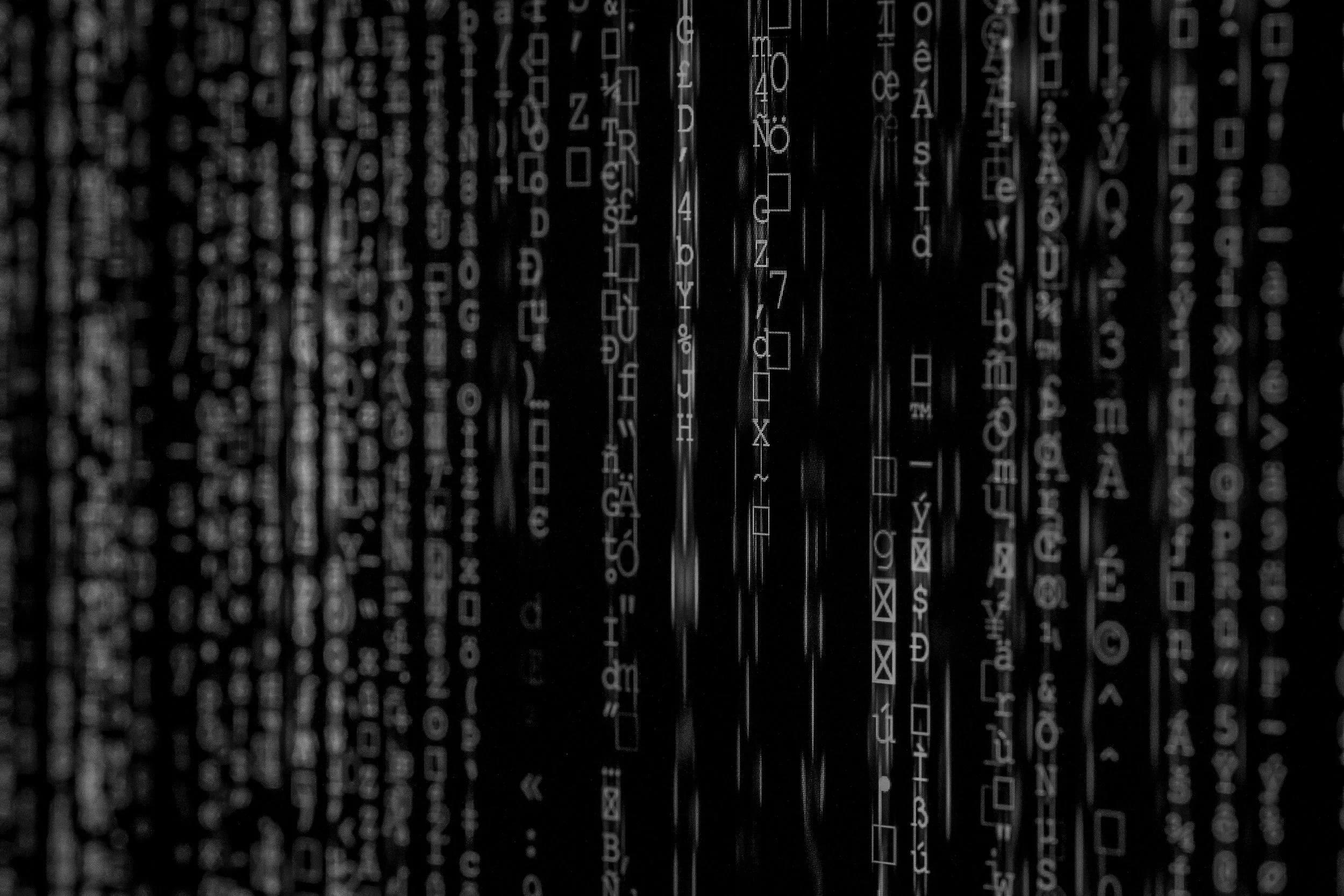 A dark image with vertical lines of white text and symbols resembling computer code or programming language.