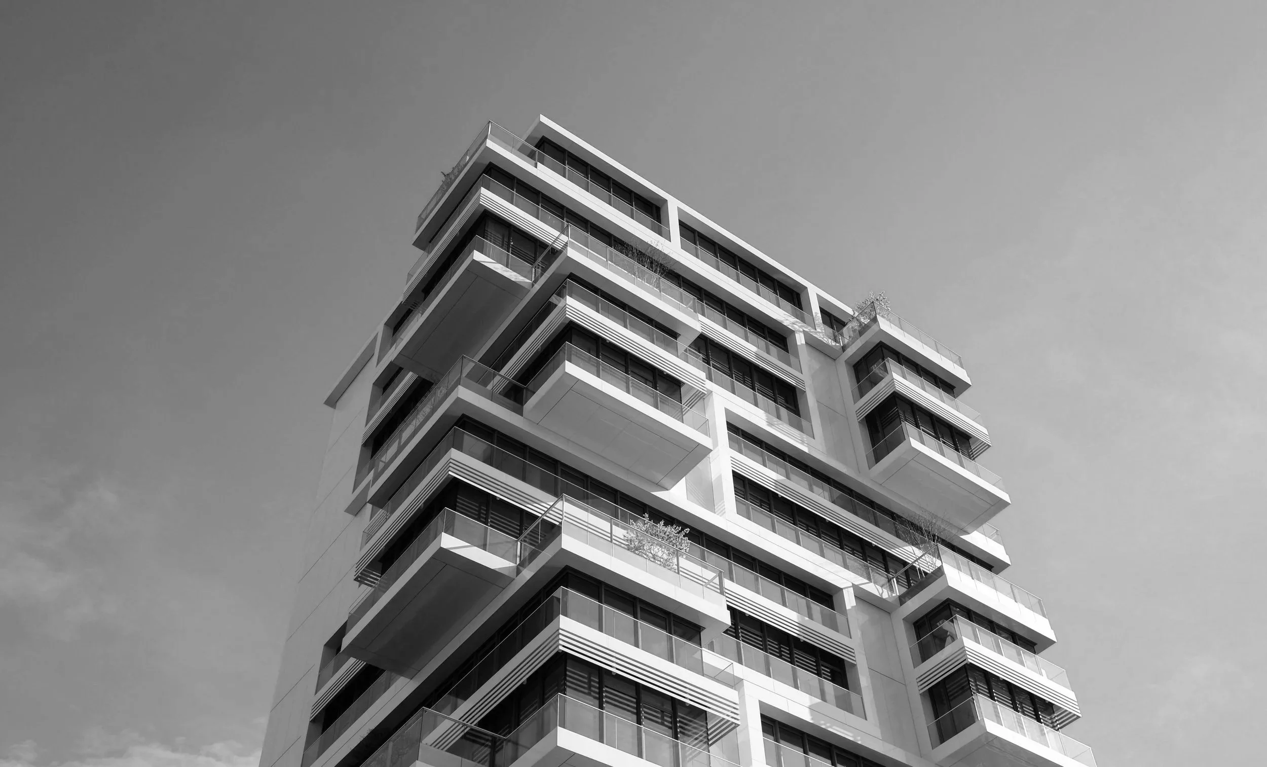A modern multi-story apartment building with balconies, set against a clear sky, in black and white.
