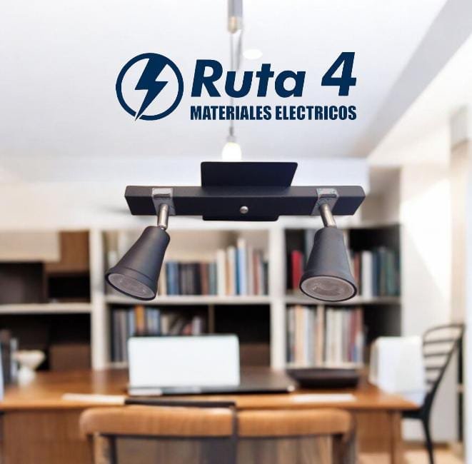Logotipo de 'Ruta 4 Materiales Eléctricos' en una oficina con mesa, sillas y estanterías con libros, visto desde abajo con foco de luz.