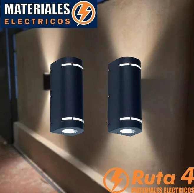 Dos focos de pared de color negro en una pared beige, con una señal de materiales eléctricos en la esquina superior izquierda que tiene un logotipo de rayo y texto en español, y una marca naranja en la esquina inferior derecha que dice 'Ruta 4 Materi