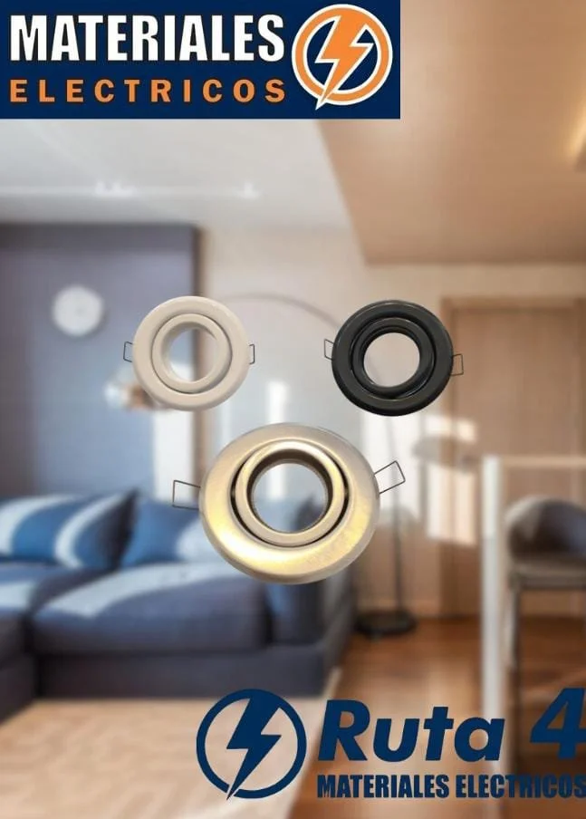 Imagen de tres focos de iluminación en diferentes colores (blanco, negro y dorado) en un entorno de sala de estar con muebles de madera y sofá, con un cartel en la parte superior que dice 'Materiales Eléctricos' y en la parte inferior 'Ruta 4 Materiales Eléctricos'.