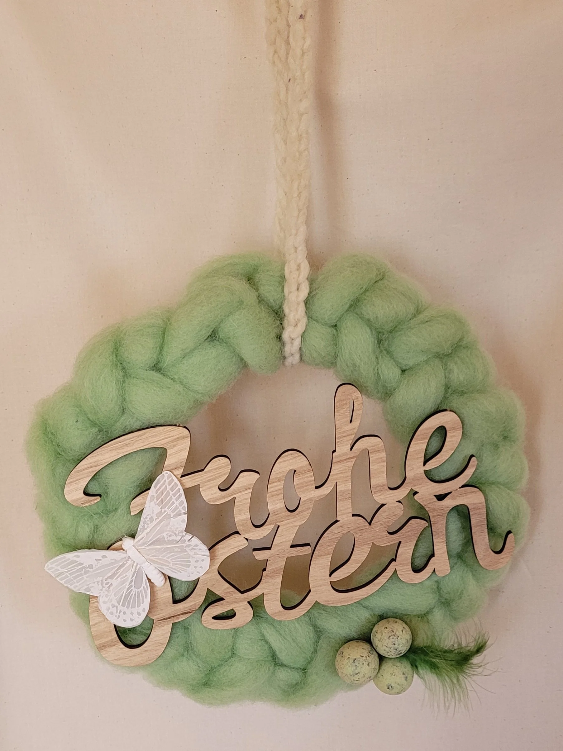 mit gefärbter Wolle geflochtener Kranz, dekoriert mit Holzschriftzug