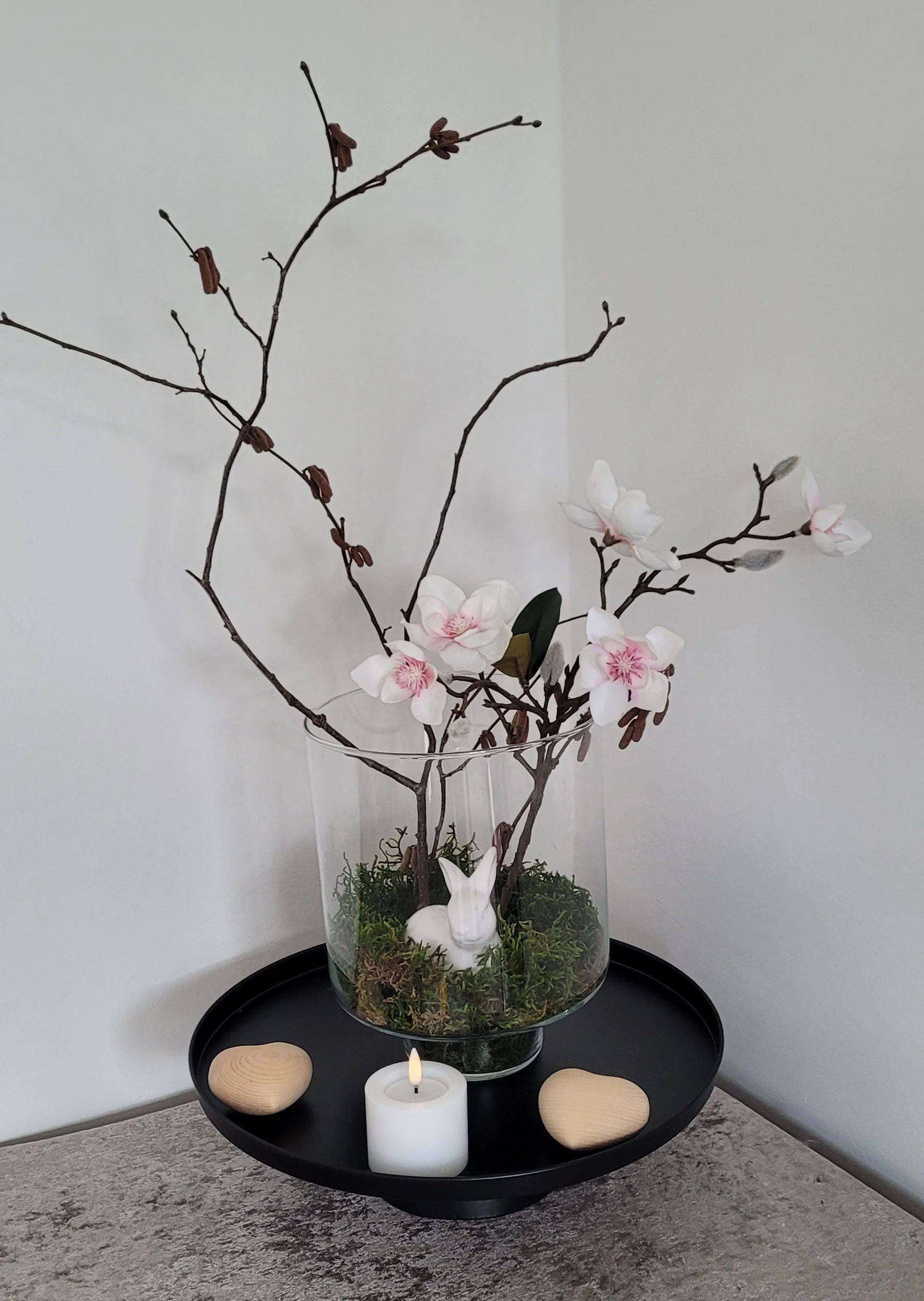 Porzellanhase mit künstlichen und echten Zweigen auf konserviertem Moos in Glasvase, dekoriert mit Zirbenholzherzen und hochwertigem LED-Teelicht, optional mit Fernbedienung