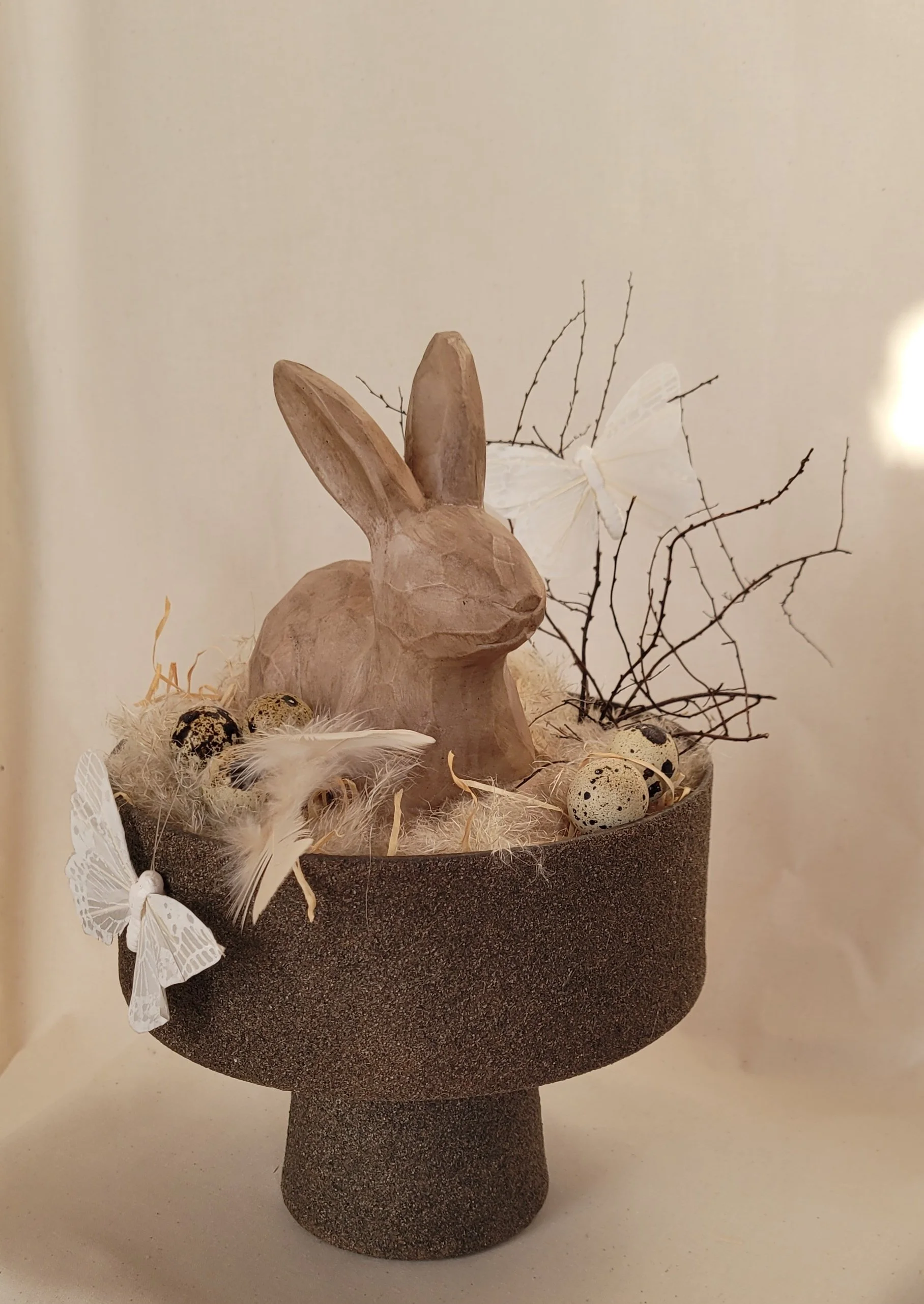 Holz-Osterhase in einer Schale aus recyceltem Papier und Holzstaub, dekoriert mit Naturmaterialien