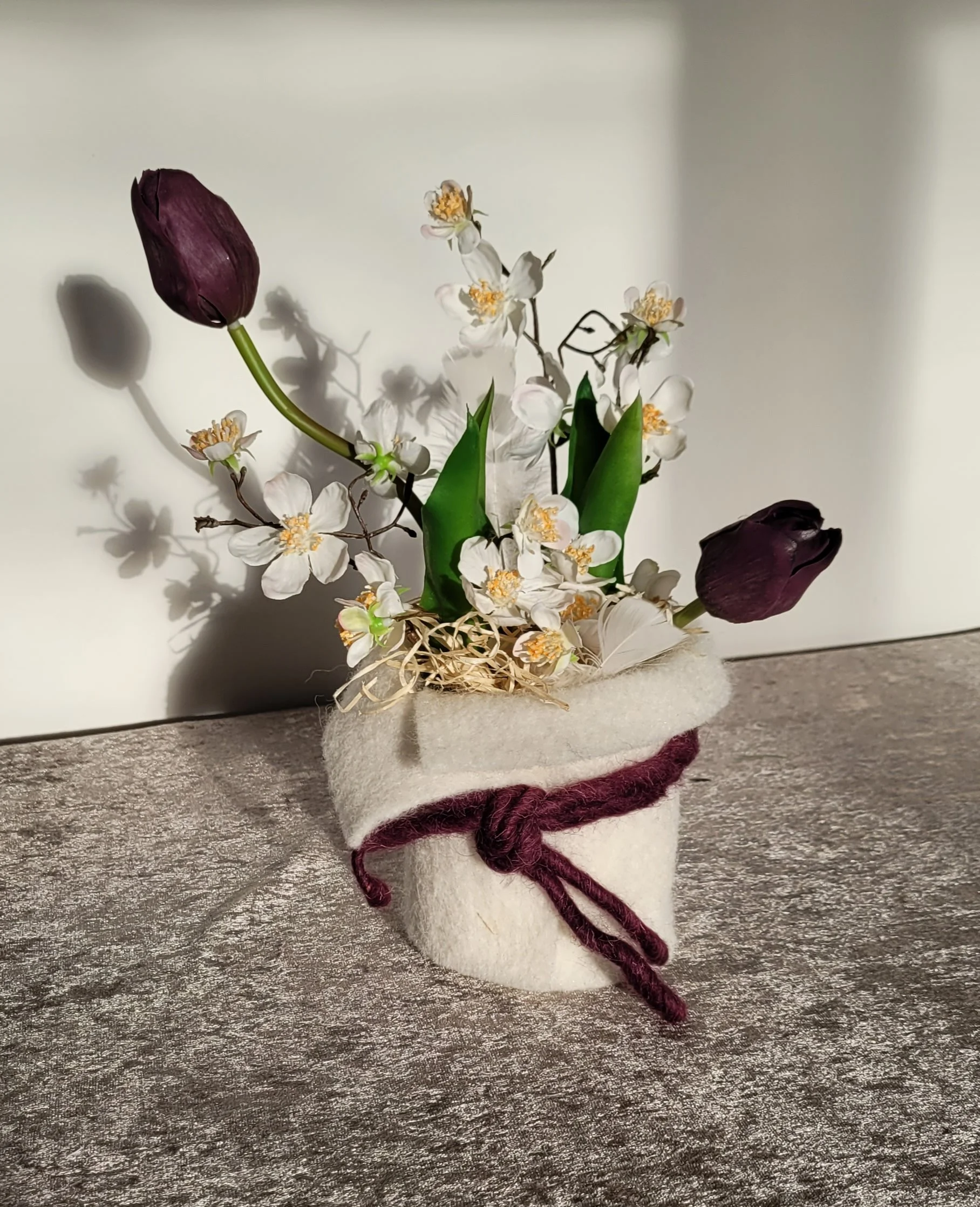Gummitulpen mit künstlichen Frühjahrsblühern im Topf, umwickelt mit Schafwollband