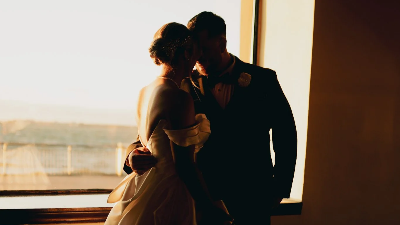 Silhouetted bride and groom close together in front of a window at sunset, sharing an intimate moment.