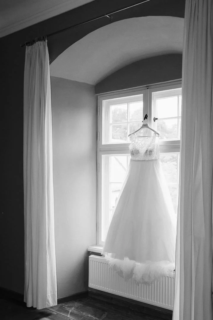 Schwarz-weiß Foto eines Brautkleides, das beim Getting Ready im Schloss Neuburg am Fenster hängt