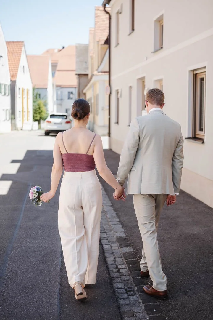 Hochzeitsfoto, das ein spazierendes Paar von hinten in der Altstadt von Friedberg (Augsburg) zeigt