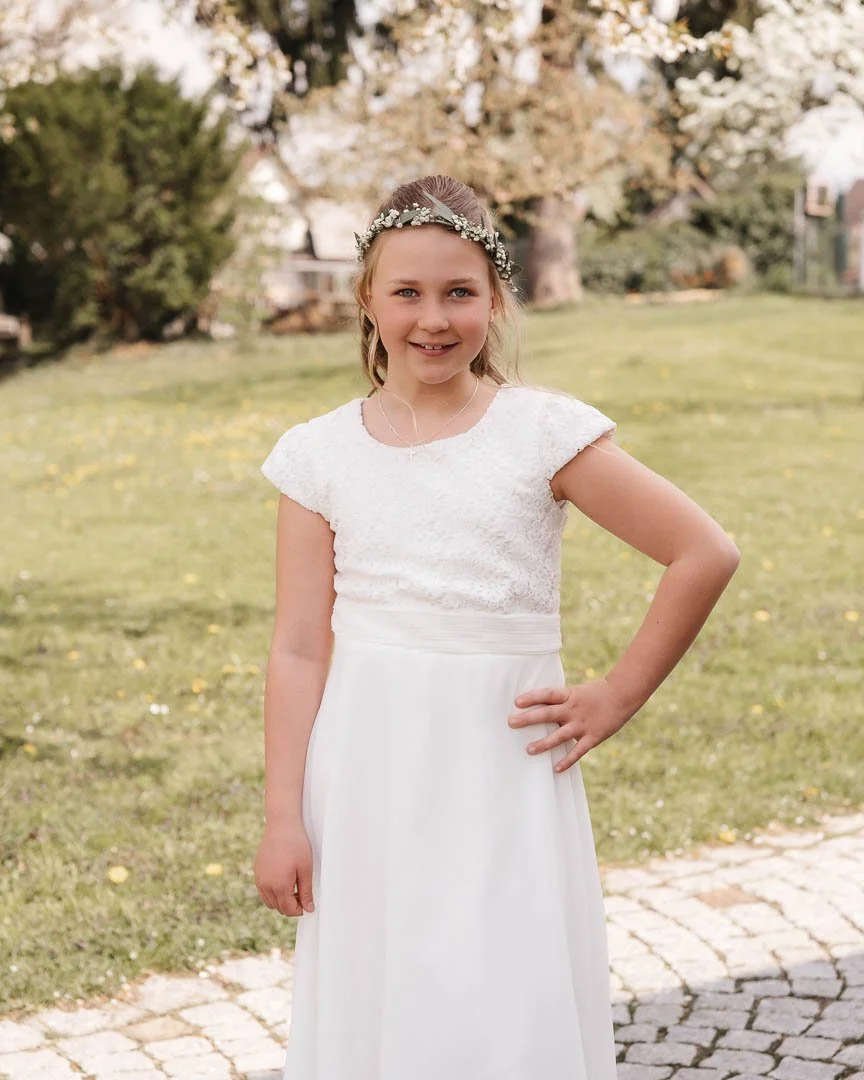 Portraitfoto eines Mädchens mit weißem Kommunions-Kleid und Blumenschmuck im Haar