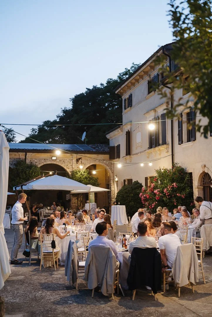 Foto einer Hochzeitsgesellschaft beim gemütlichen Zusammensitzen im Außenbereich der Hochzeitslocation Corte Marzago am Gardasee, während die Nacht hereinbricht