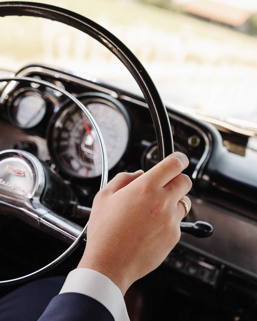 Hand eines Bräutigams mit Ehering am Lenkrad des Hochzeitsautos, ein Chevrolet Oldtimer