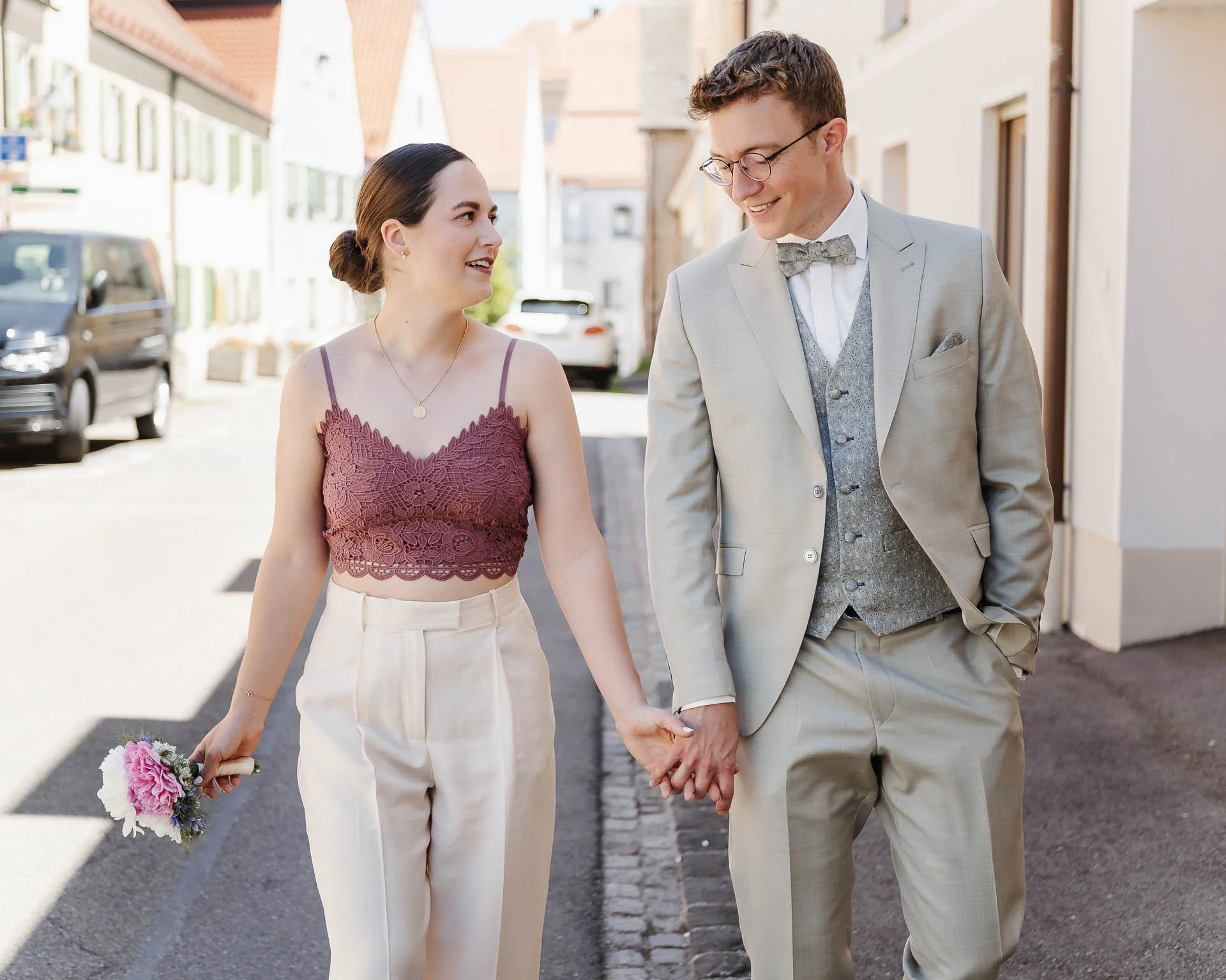 natürliches Hochzeitsfoto eines Brautpaares in modernen Hochzeitsoutfits, das locker eine Strasse in Augsburg entlang geht