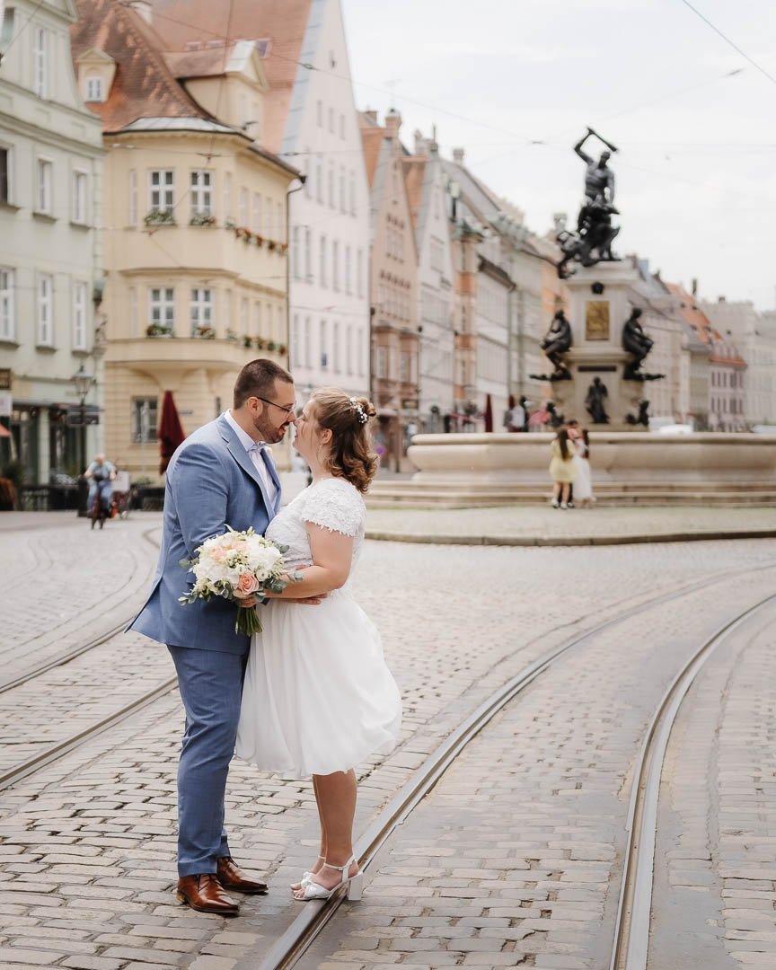 Foto eines Brautpaares, das sich in der Maxstraße Augsburg vor dem Herkulesbrunnen küsst