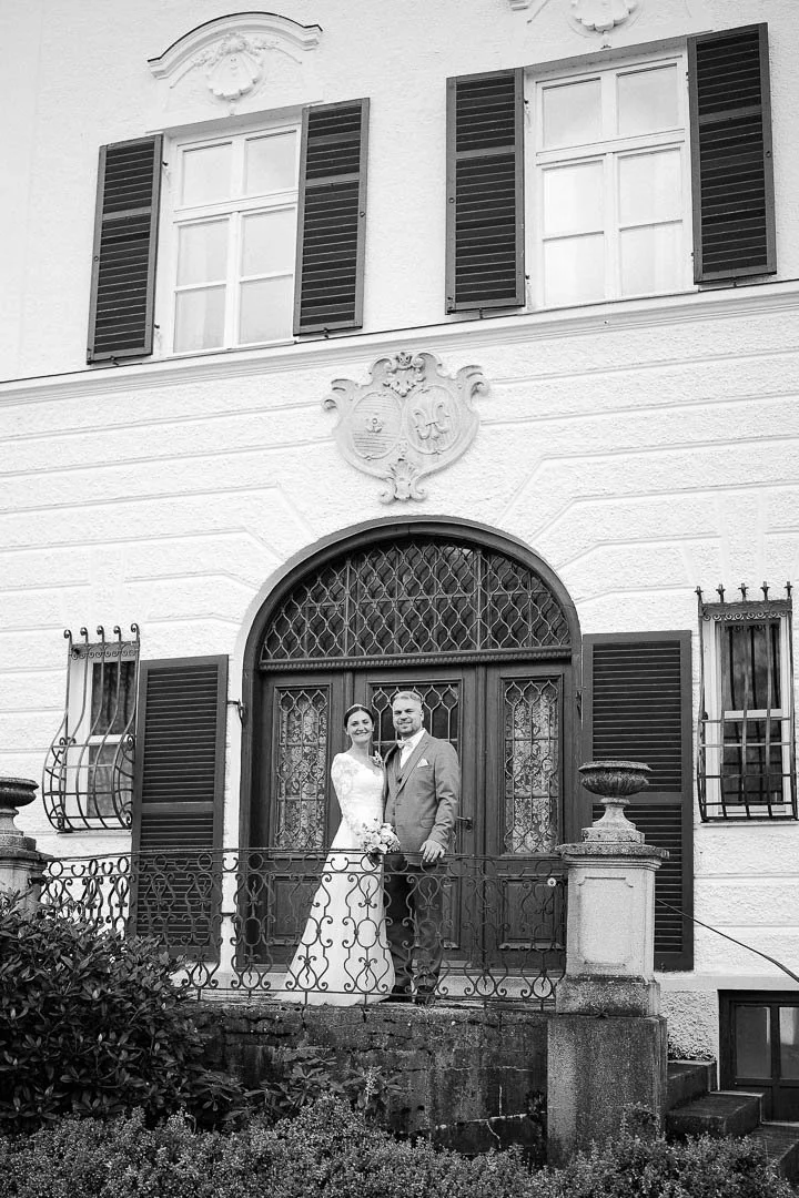 Schwarz-weiß Hochzeitsfoto eines Brautpaares vor einem historischen Anwesen bei Augsburg