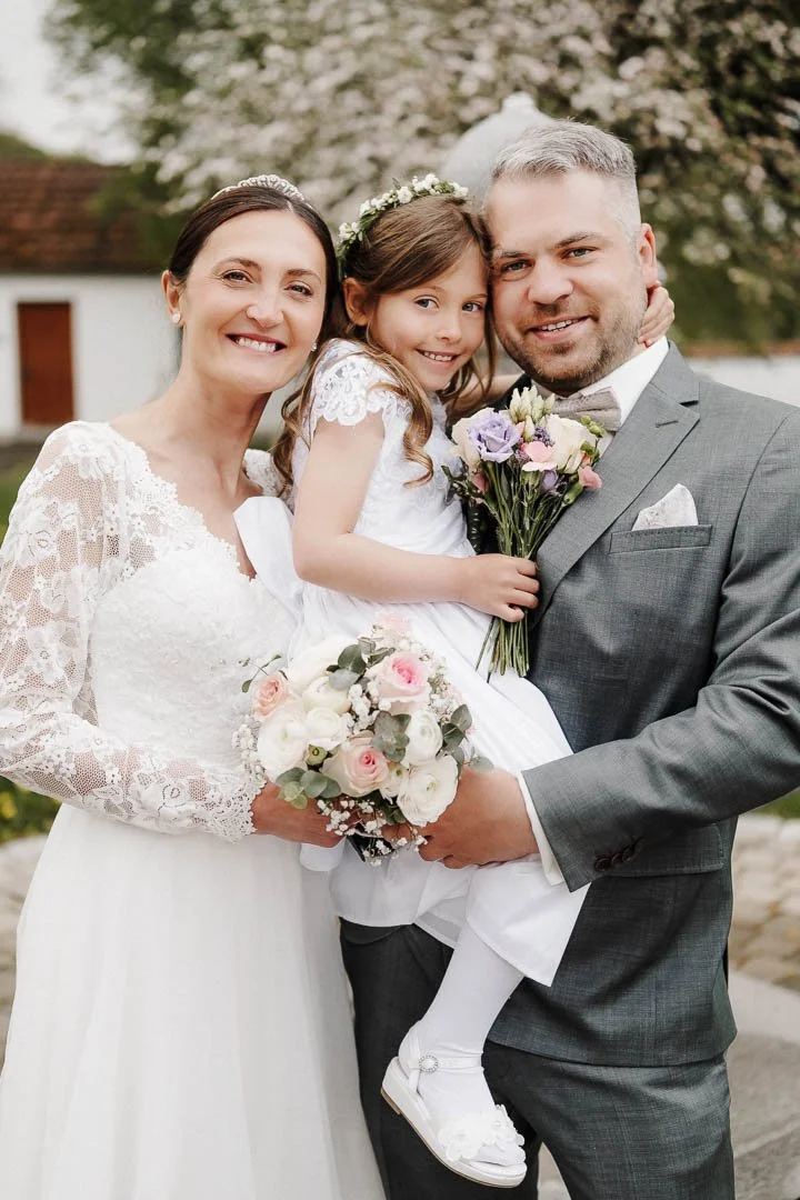 Brautpaar mit Tochter und Brautstrauß beim lockeren Fotoshooting nach der Trauung in Fischach (Region Stauden)