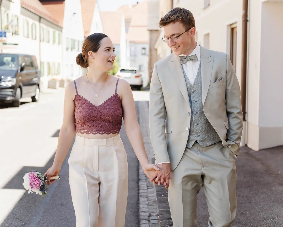 natürliche Hochzeitsfotografie, die ein Paar händehalten beim Spazierengehen in Augsburg zeigt, während sich das frisch verheiratete Paar locker unterhält
