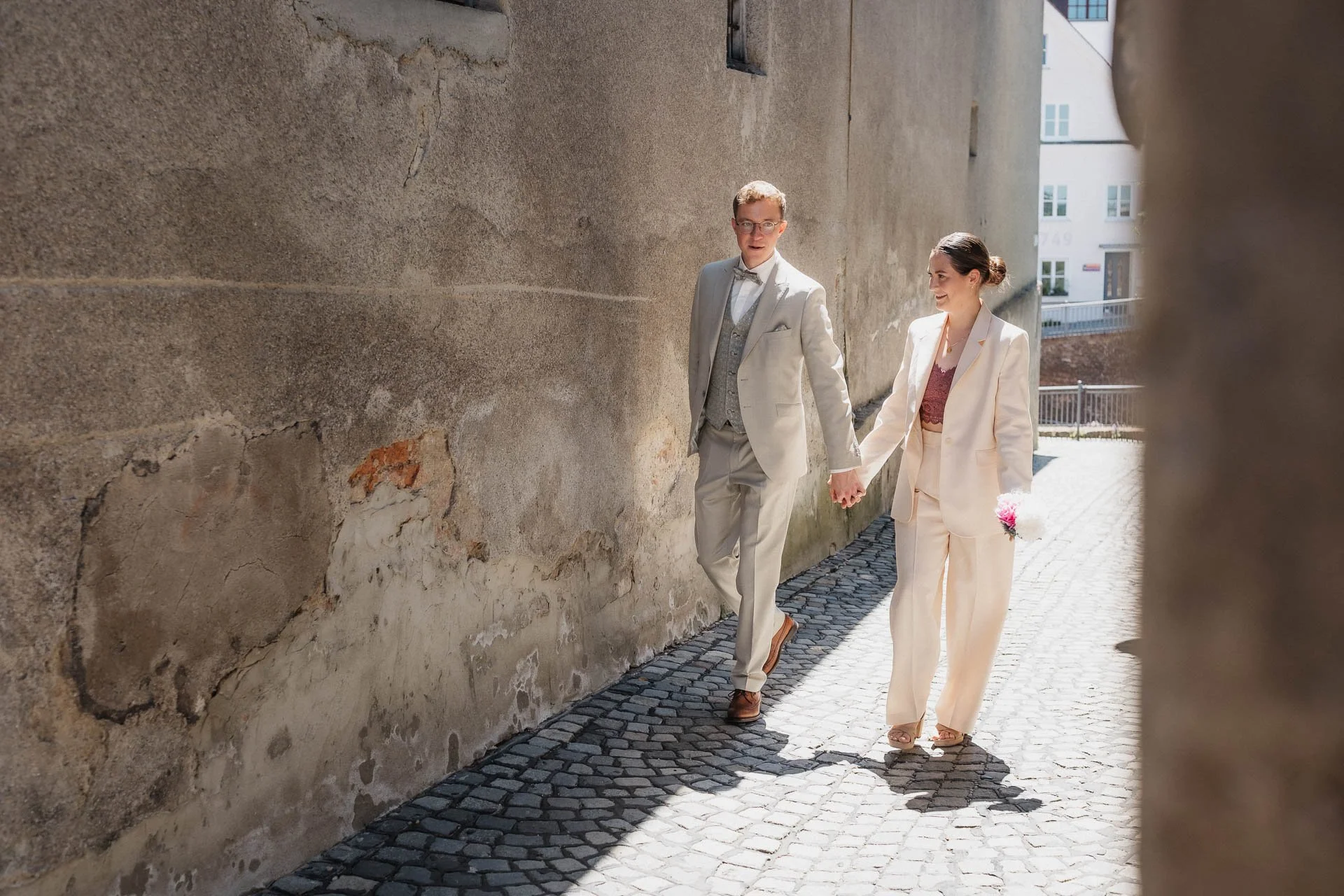 sommerliches Hochzeitsfoto, auf dem ein Brautpaar lässig durch eine enge Gasse in der Altstadt von Augsburg schlendert