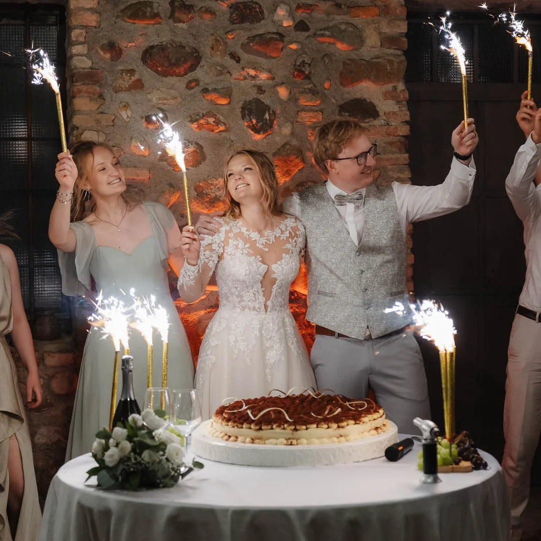 Ein Brautpaar aus München steht mit Gästen vor ihrer Hochzeitstorte im Außenbereich einer Villa in Italien, währen alle Feuerwerks-Fontänen in den Händen halten